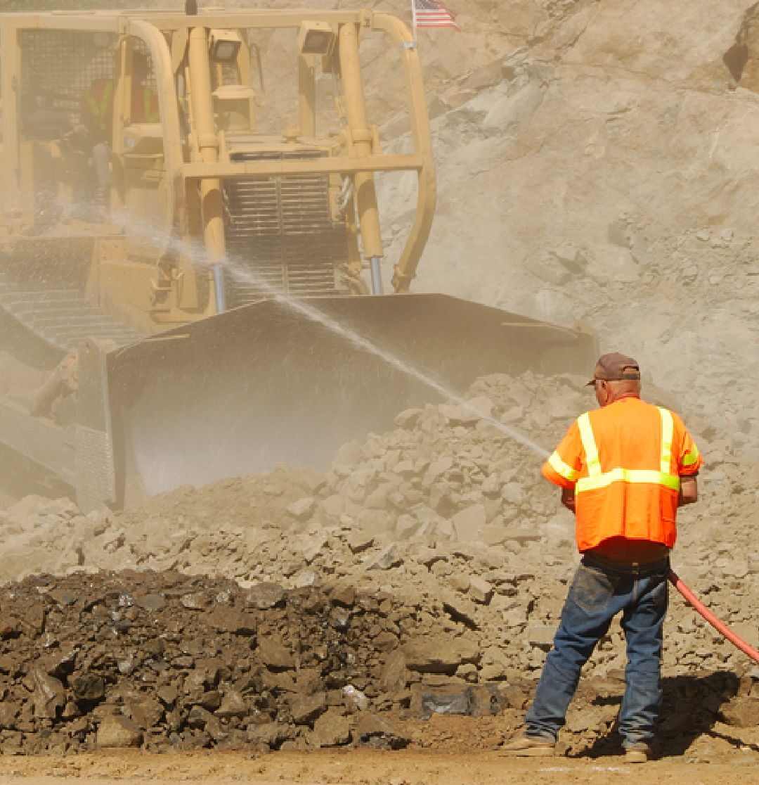 A man at a construction site using a water hose as demolition dust control equipment