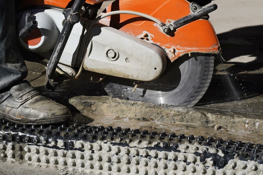Workers using a concrete saw to cut through a monolithic slab at a construction site in bright sunlight day. 