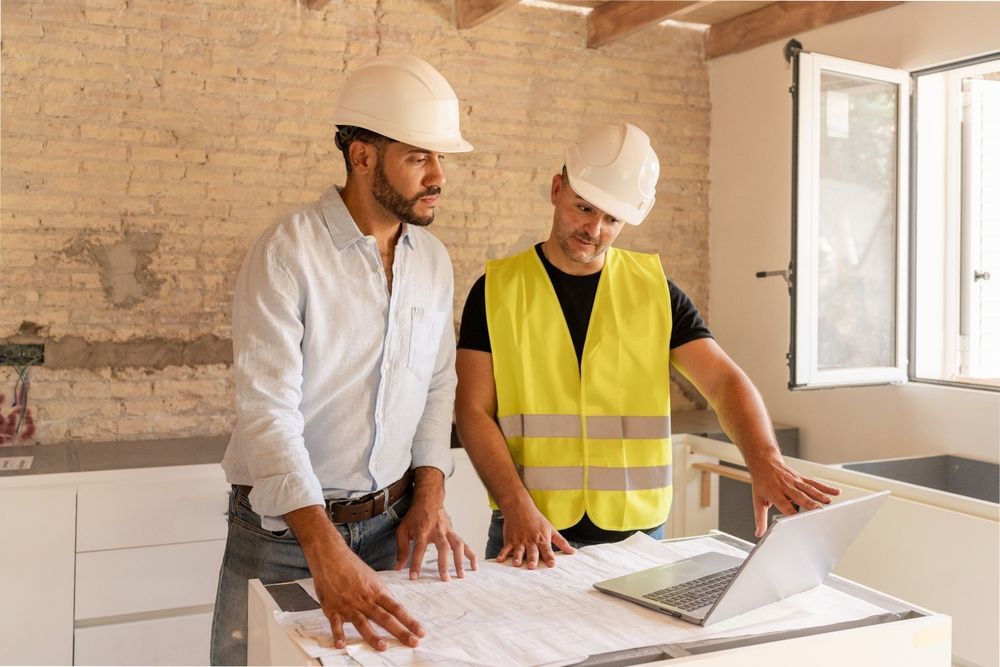 Architect and contractor discussing bid package plans on laptop during renovation project