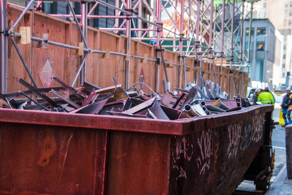 Dumpster logistics with roll off container full of metal scrap at urban construction site with scaffolding and fencing