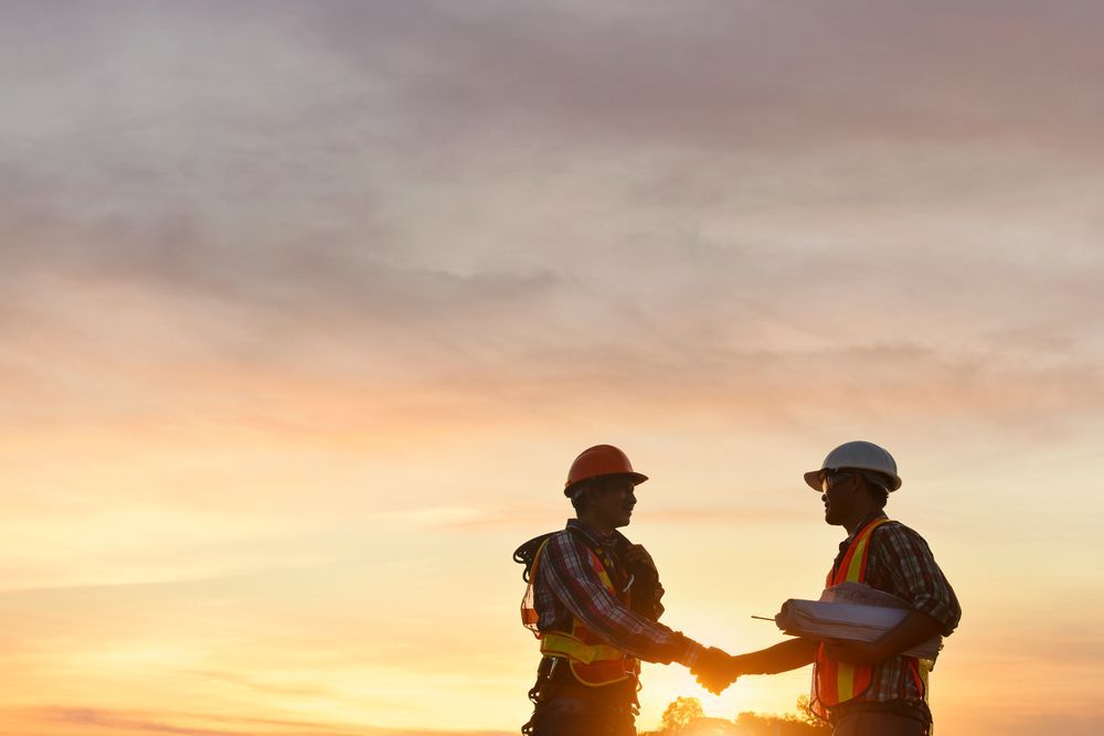 General Contractor and building inspector shaking hands on site while reviewing blueprints and supervising construction progress