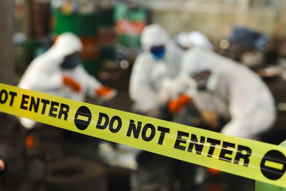 HAZMAT investigation at chemical plant with officials in protective gear behind do not enter barrier tape marked no trespassing