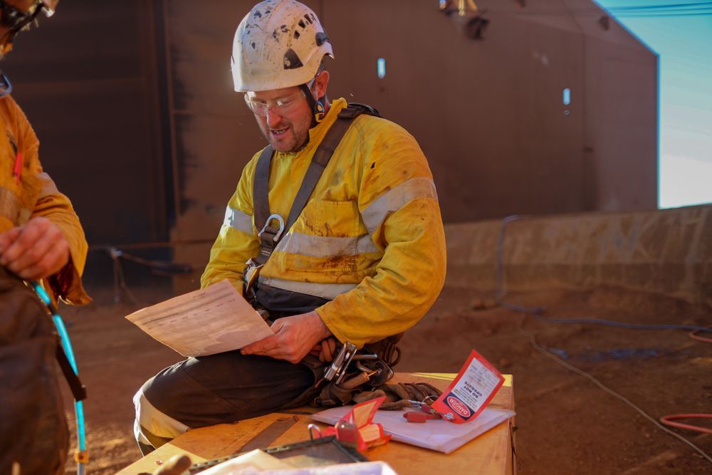Miner wearing a white fall protection safety helmet double checking on JHA Job Hazard Analysis before signing signature permit to work prior work on opening field construction mine site Australia 