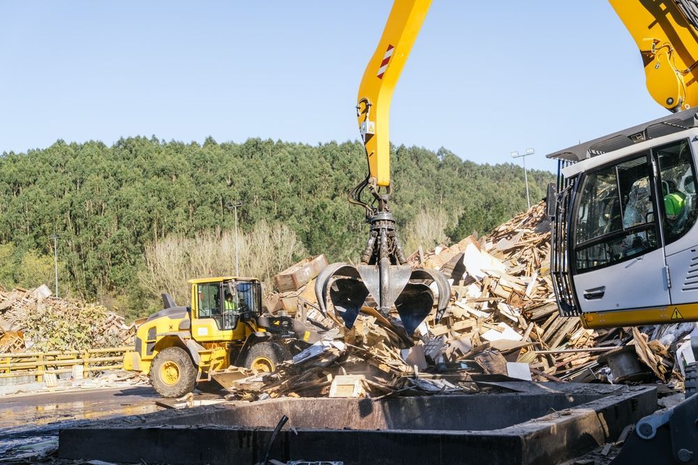 Recycling rate improvement with material handler claw picking up wood waste at recycling facility