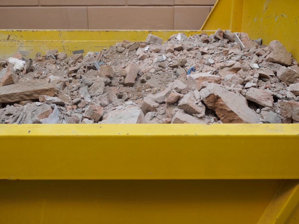 Rubble removal with yellow dumpster overflowing with construction debris and concrete at demolition site