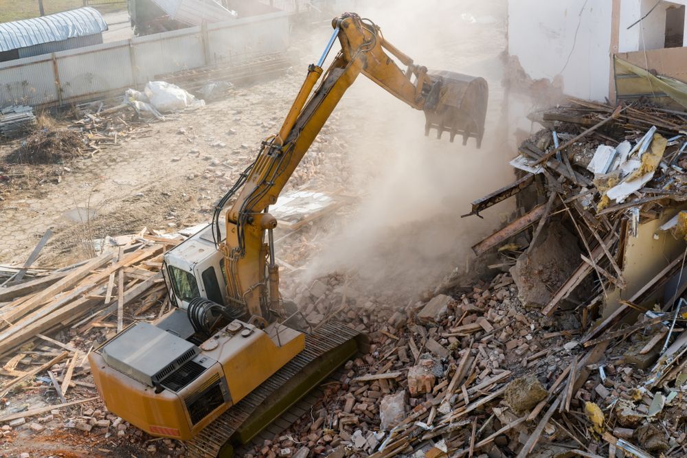 a large yellow excavator with demolition dust around it