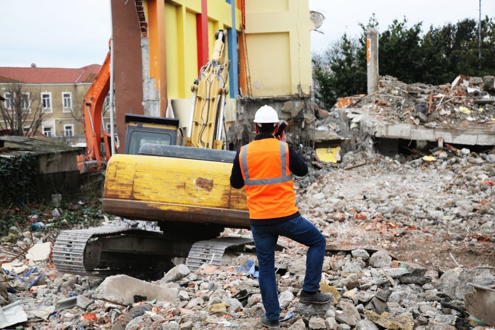 A construction worker is taking a picture of a building being demolished 