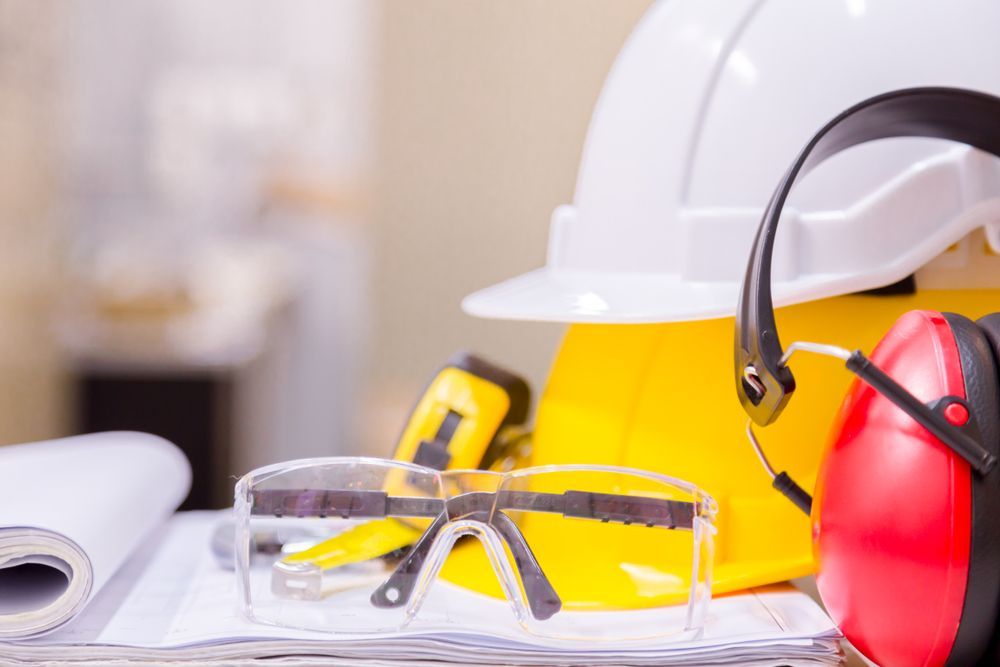 Construction safety equipment, including hard hat, safety glasses, ear protection, and blueprints.