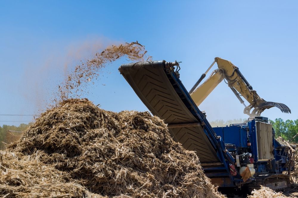 A large pile of hay is being shredded by a machine.