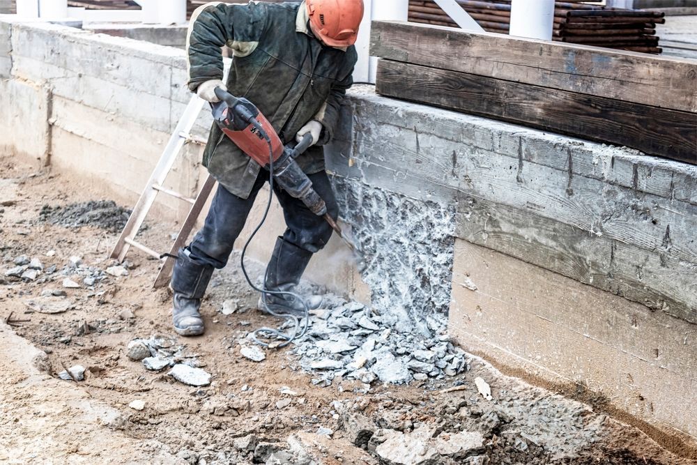 A construction worker is using a hammer to break up concrete.