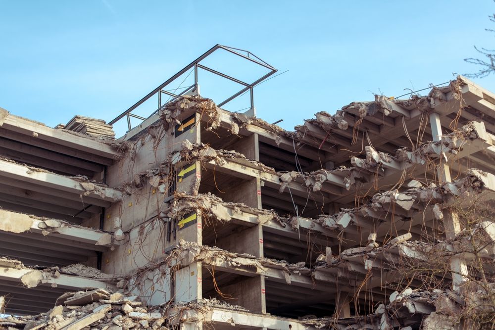 A large building is being demolished with a blue sky in the background.