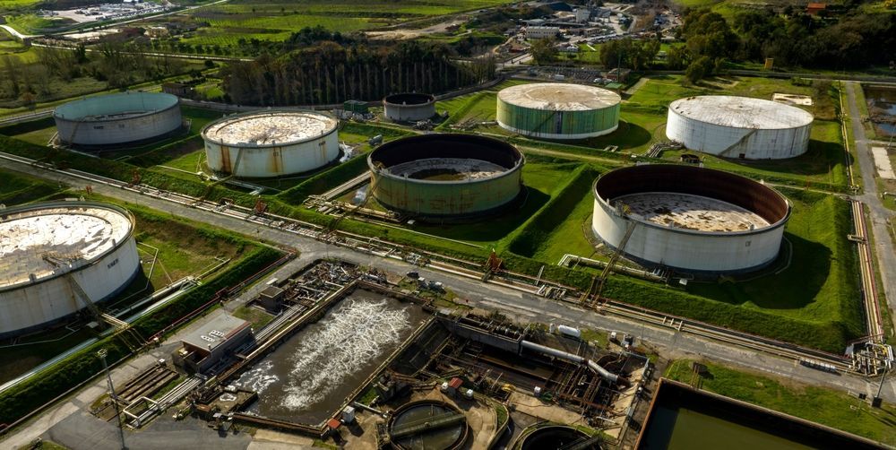 Aerial view of an oil or fuel storage facility, with several large cylindrical tanks surrounded by grass.