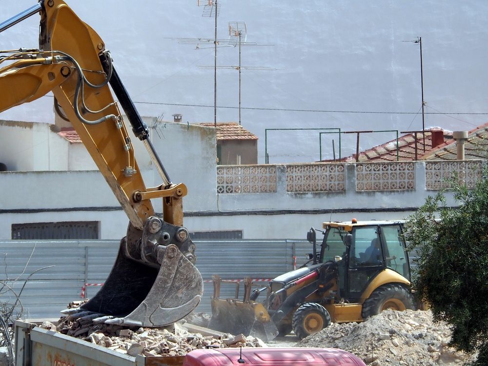 A yellow excavator is loading bricks into a dumpster