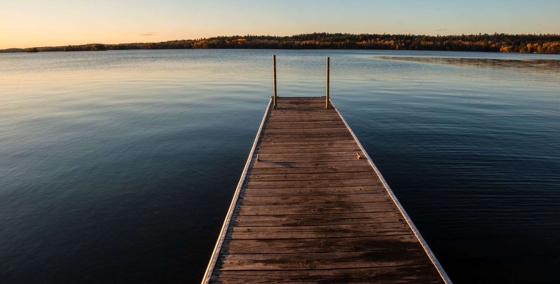a wooden dock leading into a lake at sunset .