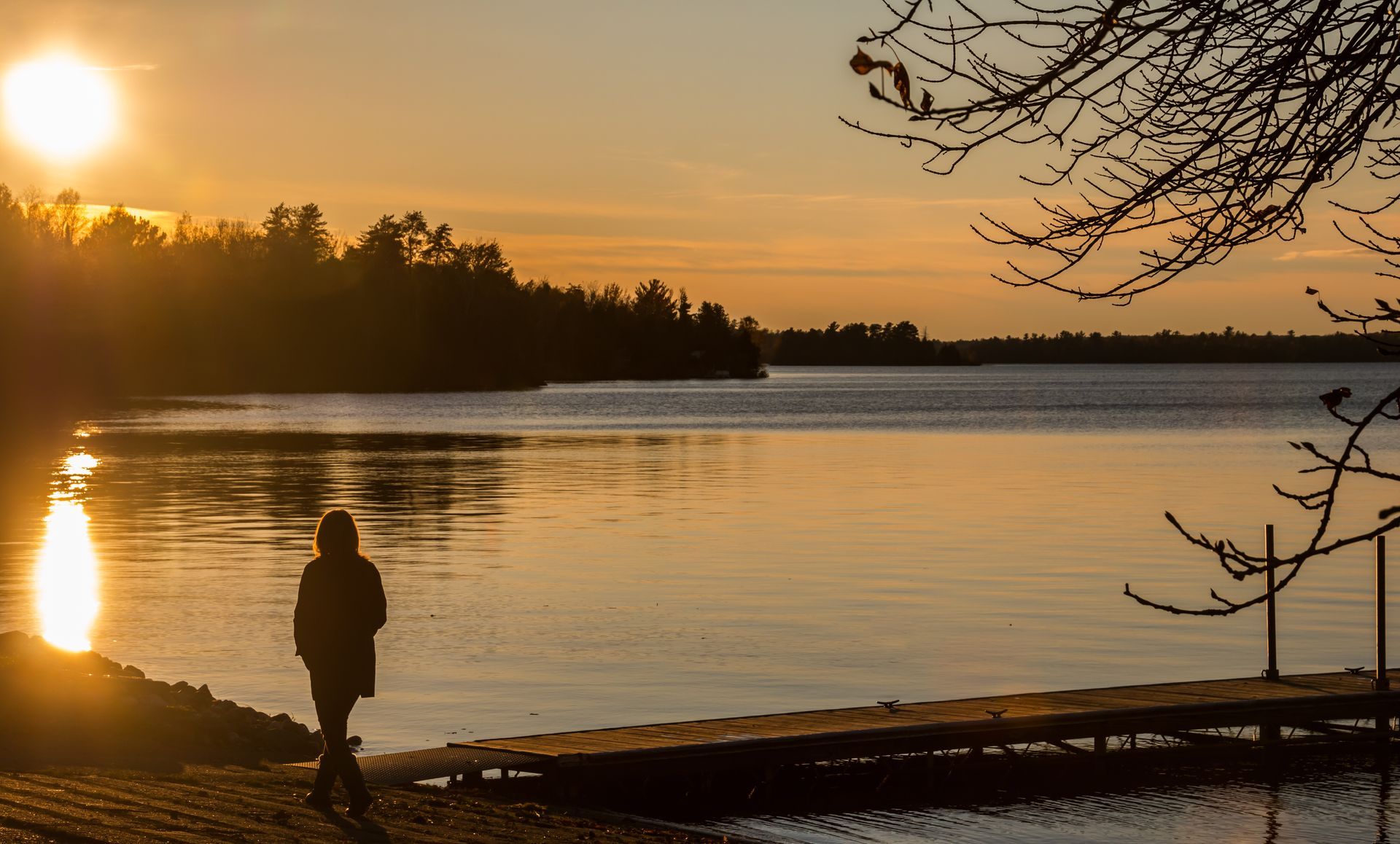 a person is standing on a dock near a lake at sunset .