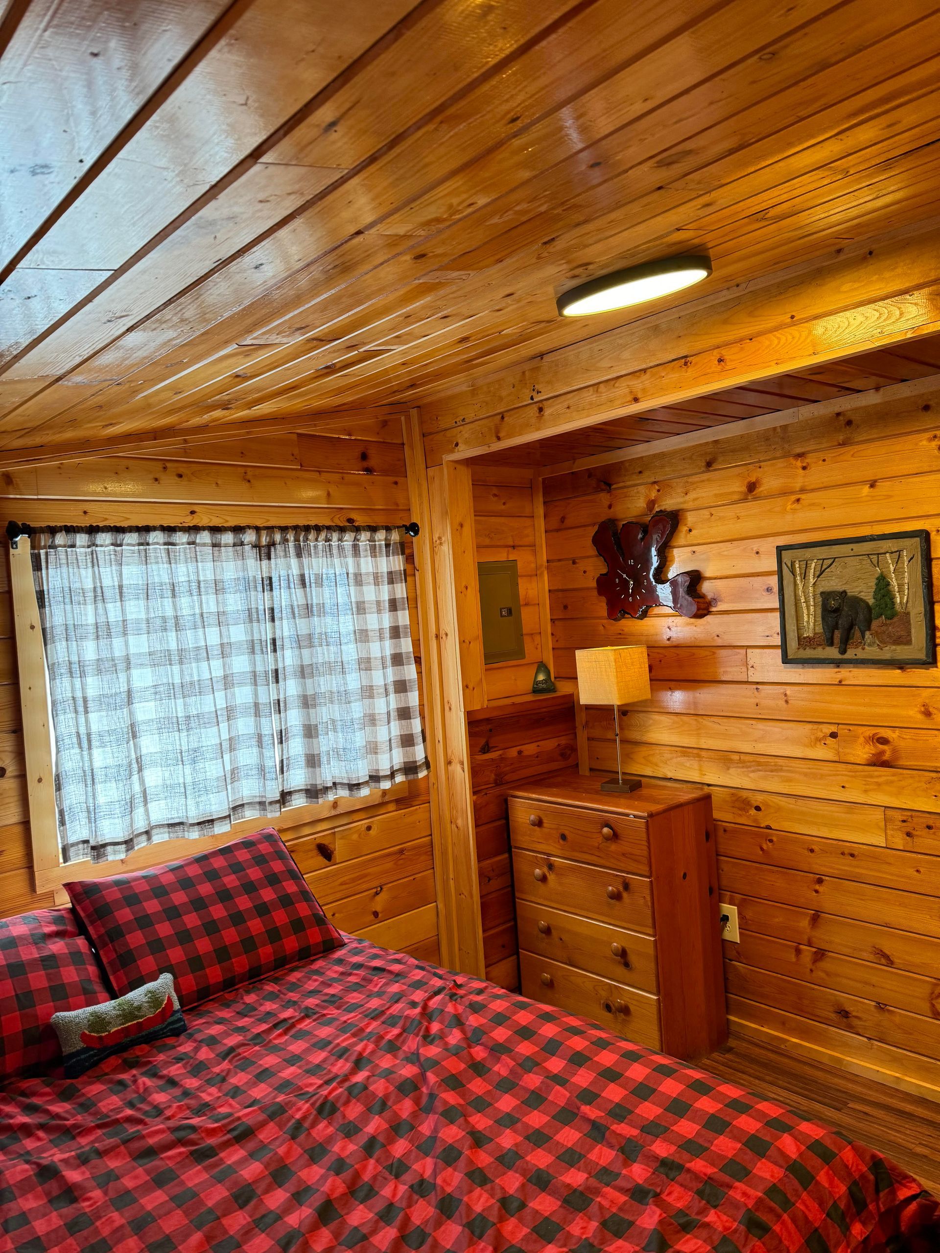 a bedroom in a log cabin with a bed , dresser , lamp and window .