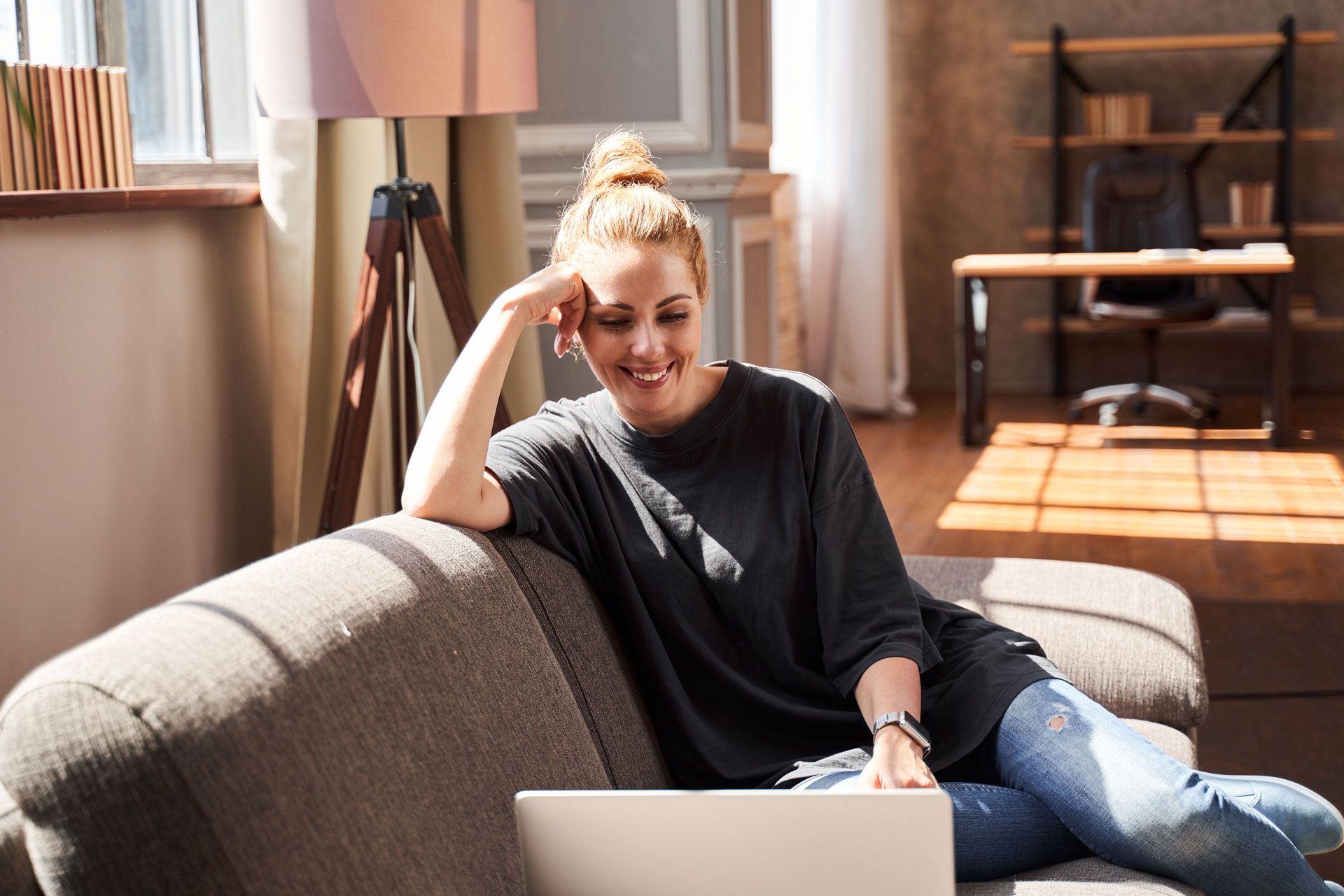 Person lounging on a couch with a laptop in a sunlit living room