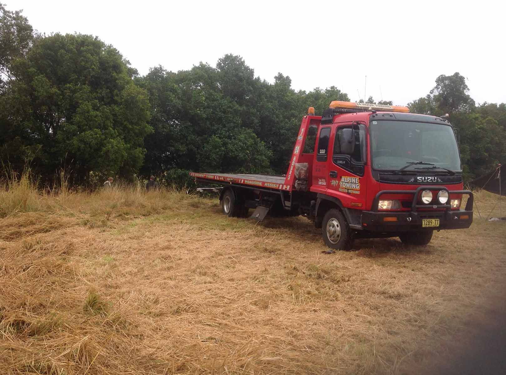 A Red Tow Truck Is Parked In A Field With Trees — Alpine Towing Services in Ballina, NSW