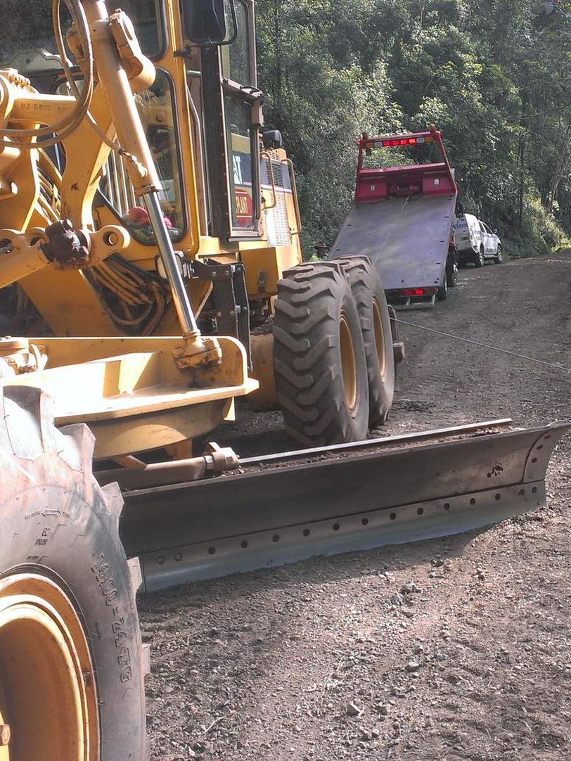 A Tow Truck Is Carrying An Agricultural Grader Up Hill — Alpine Towing Services in Lismore, NSW.