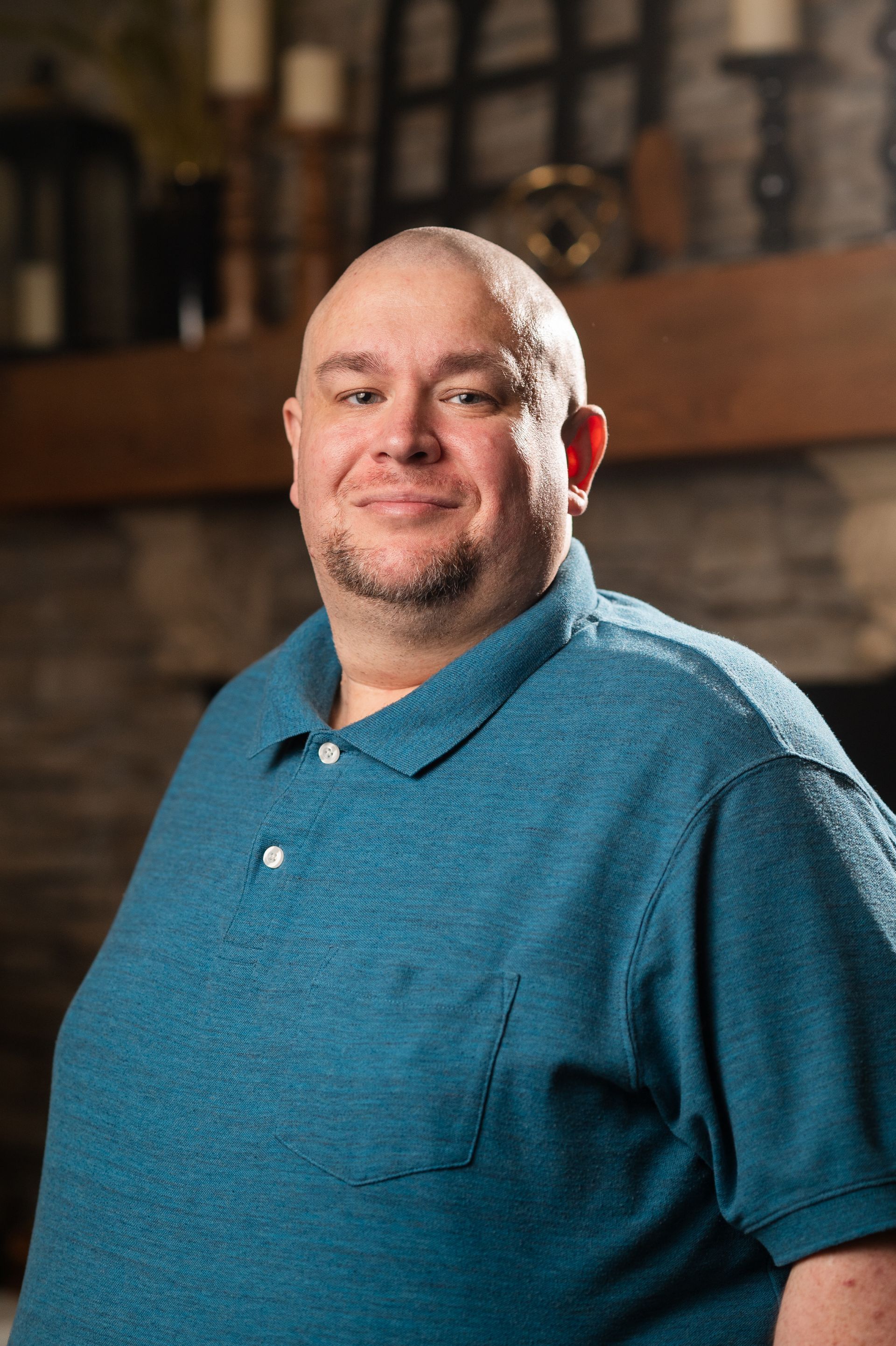 A man in a blue shirt is standing in front of a fireplace.
