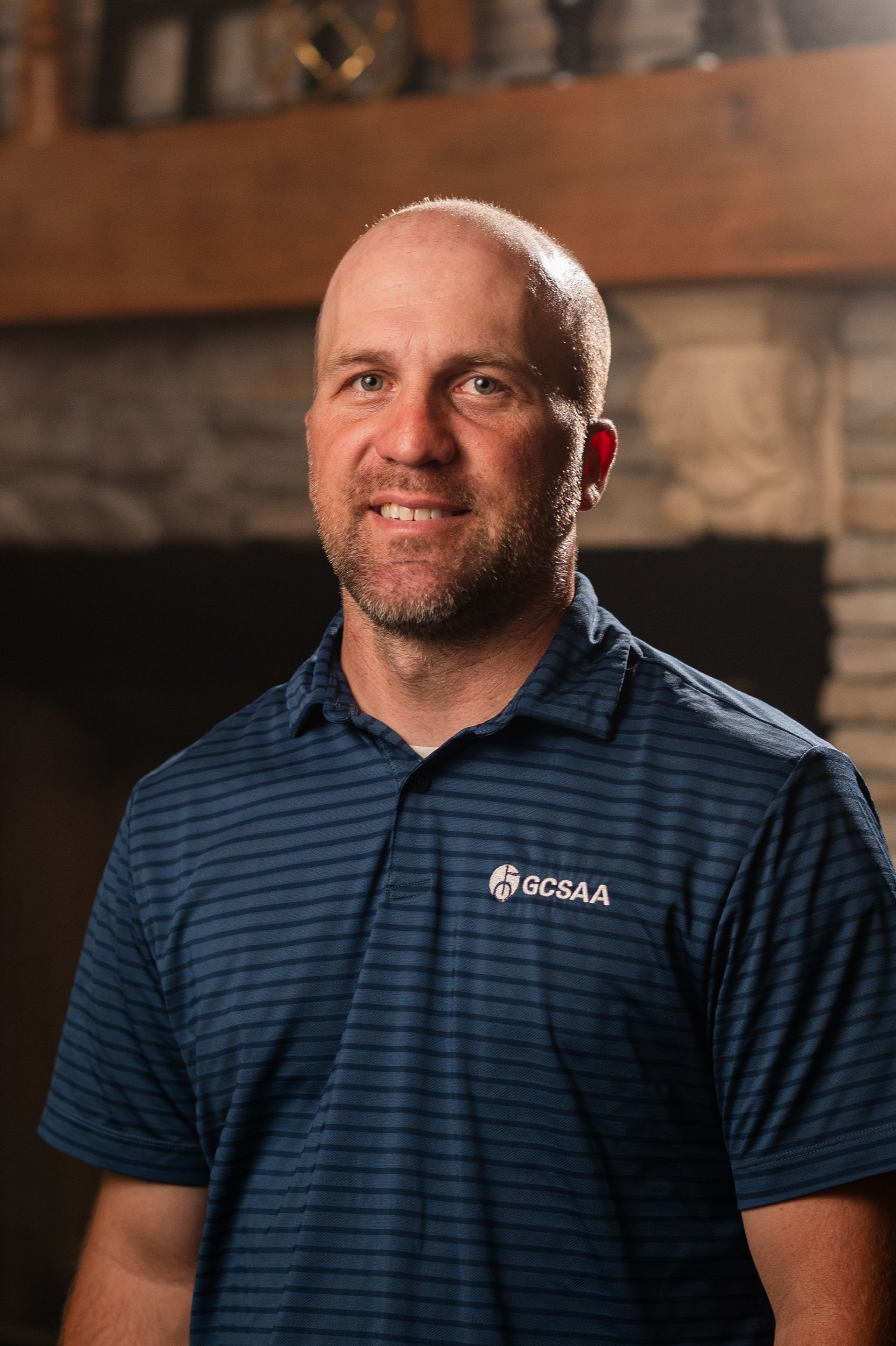 A man in a blue striped shirt is standing in front of a fireplace.