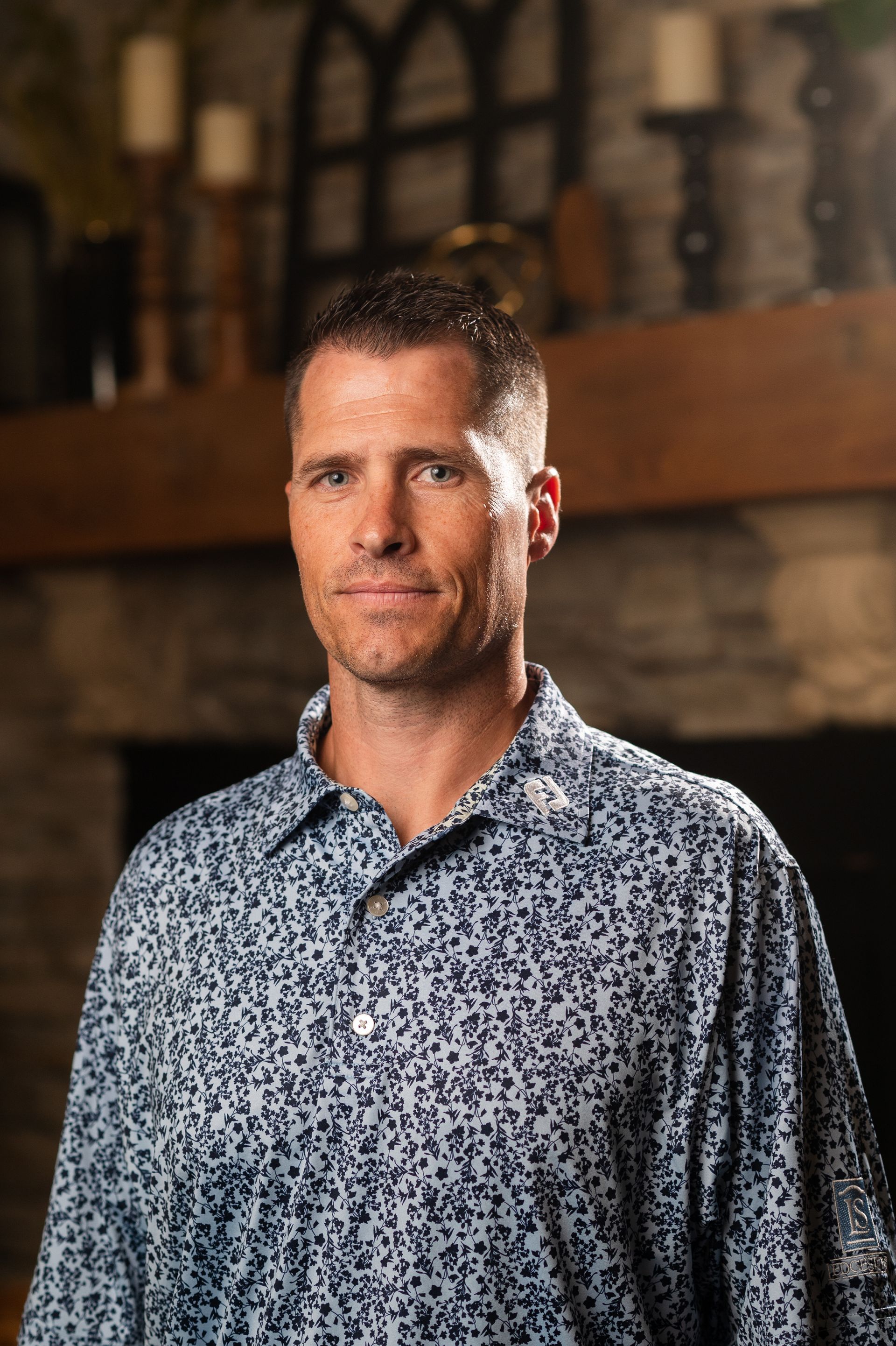 A man in a blue shirt is standing in front of a fireplace.