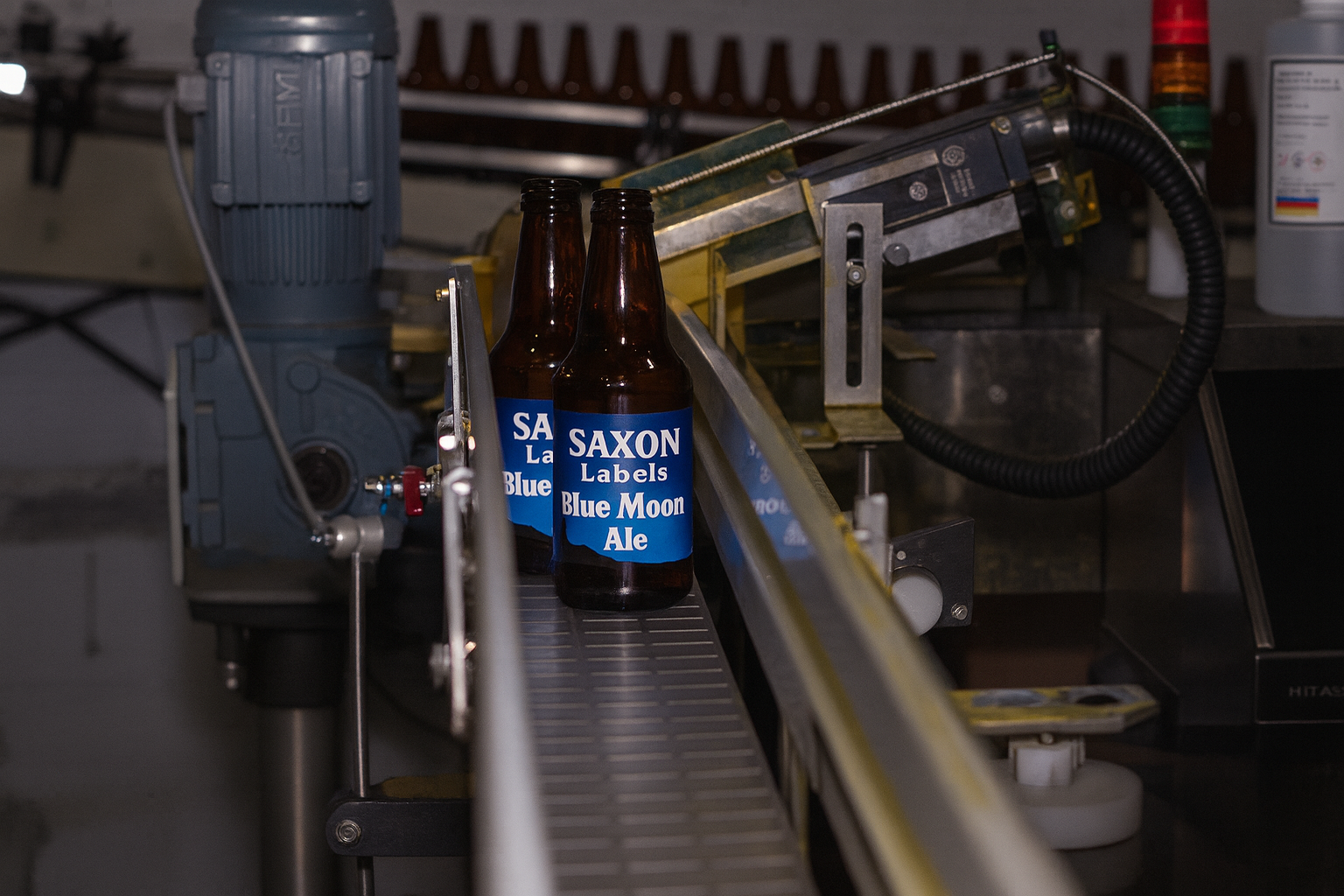Brown beer bottles with blue labels labeled "Saxon" on a conveyor belt in a factory.