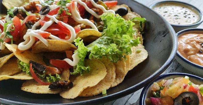 A plate of nachos with tomatoes , lettuce , olives and mayonnaise on a table.