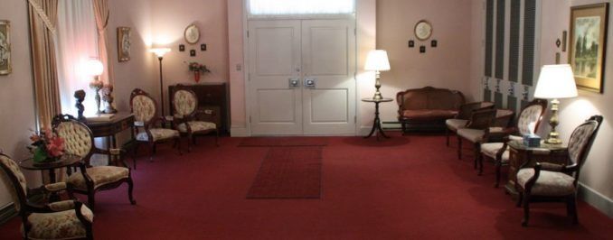 Formal sitting area with pink walls, red carpet, white double doors, and several patterned armchairs and lamps.