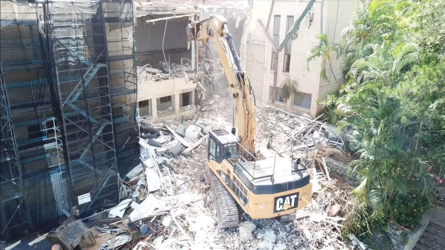 An aerial view of a cat excavator demolishing a building.