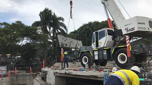 A crane is lifting a piece of concrete over a bridge.