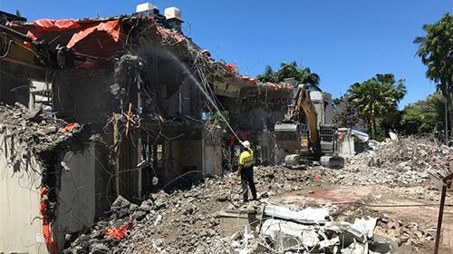 A man is spraying water on a building that is being demolished.