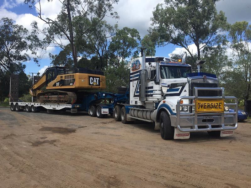 A large semi truck is carrying a cat excavator on a trailer.