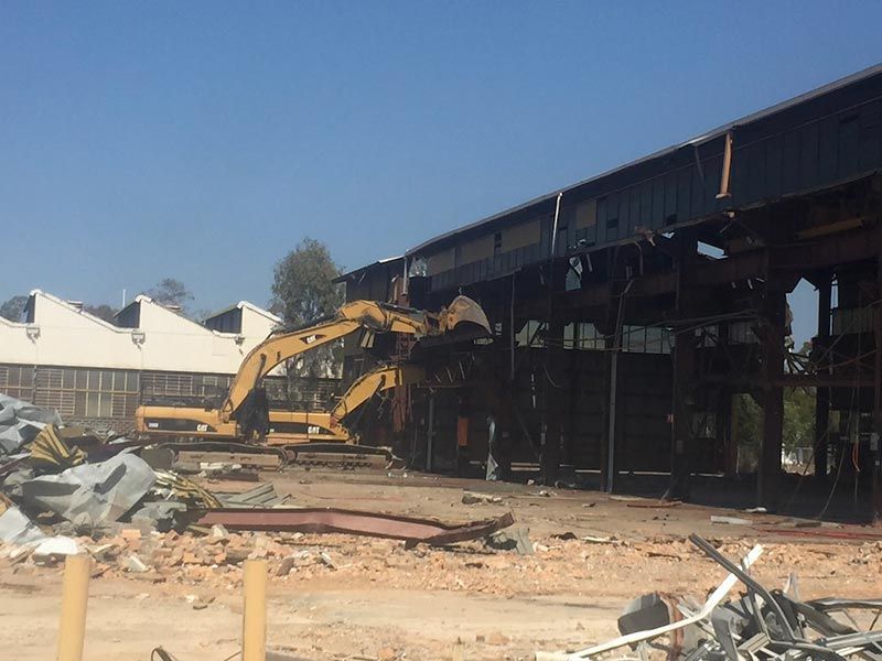 A large building is being demolished by a yellow excavator.