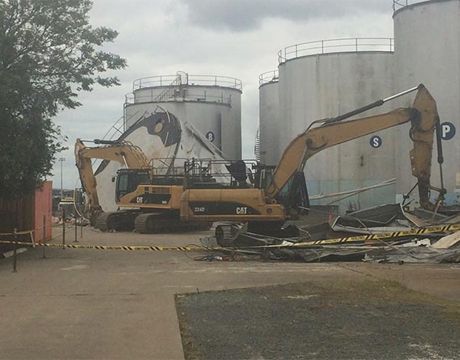 A couple of excavators are sitting in front of a large tank.