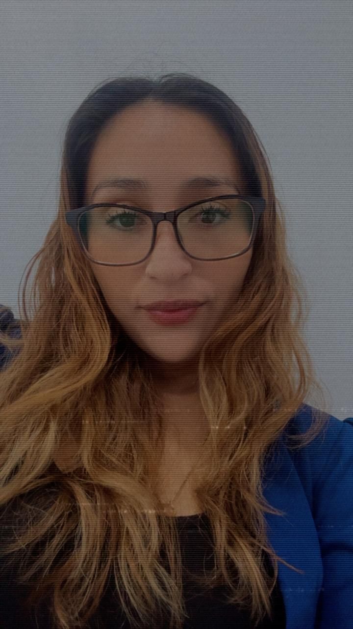 Woman with glasses wearing a blue blazer, looking directly at the camera with a neutral expression.