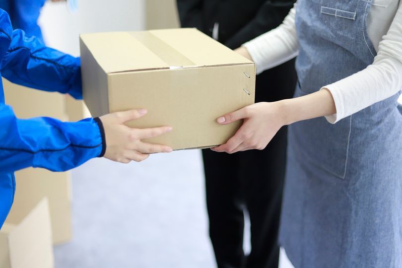 Il fattorino in uniforme blu porge una scatola di cartone a una persona con il grembiule blu.