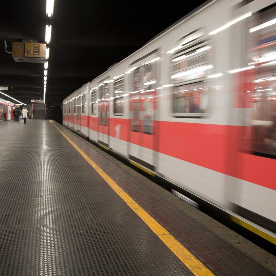 Un treno della metropolitana in una stazione con vagoni rossi e bianchi che sfrecciano oltre una linea gialla.