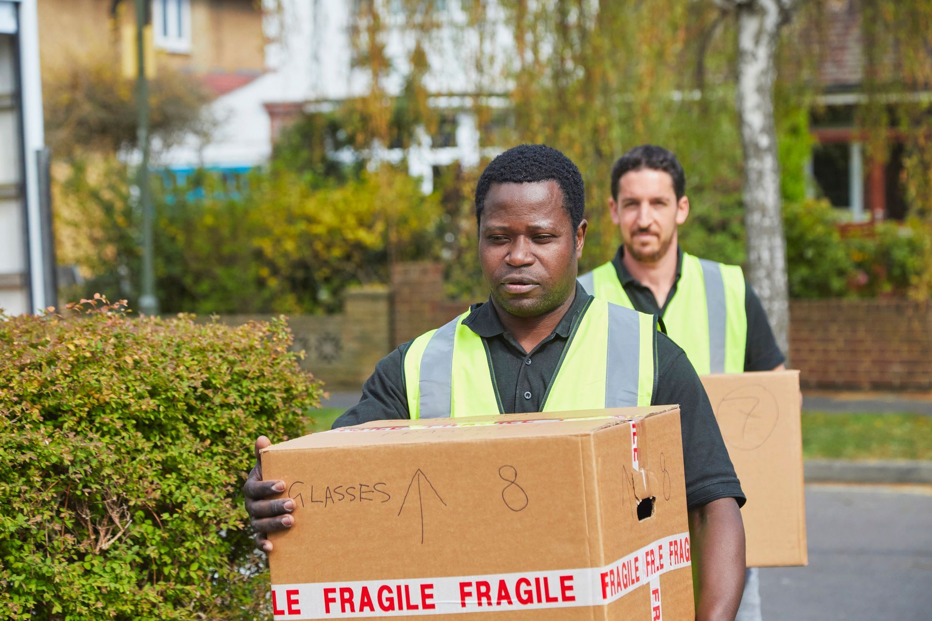 A man in a yellow vest is carrying a cardboard box.