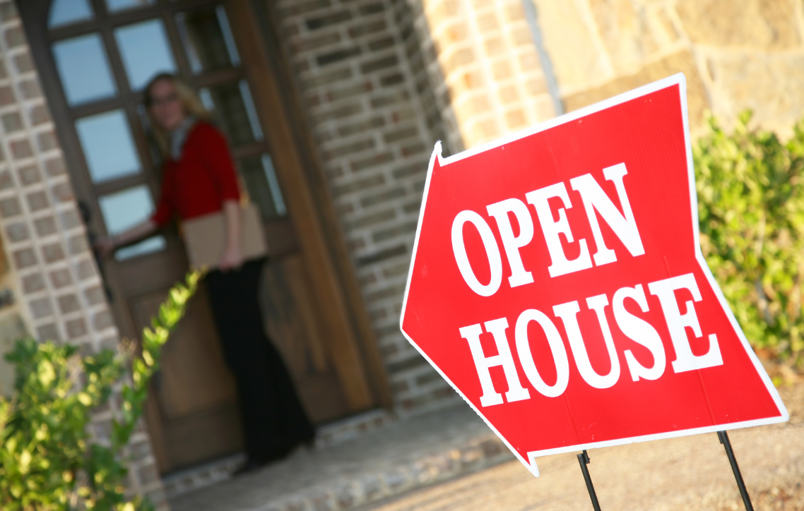 Red open house sign outside a home with a person standing in the doorway.