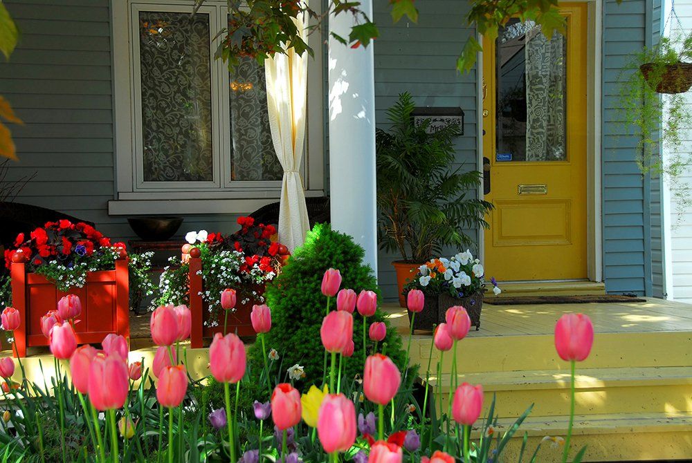 A blue house with a yellow door and flowers in front of it