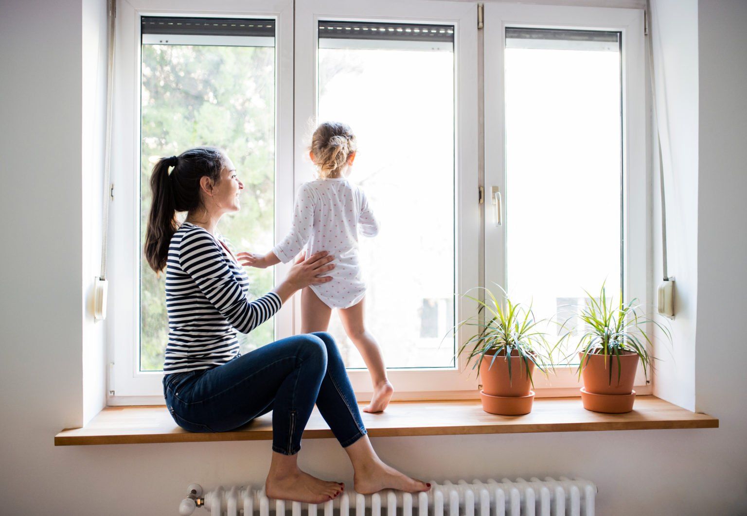 A woman and child are sitting on a window sill looking out the window.