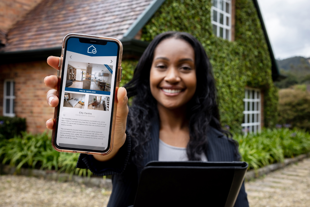 A woman is holding a cell phone in front of a house