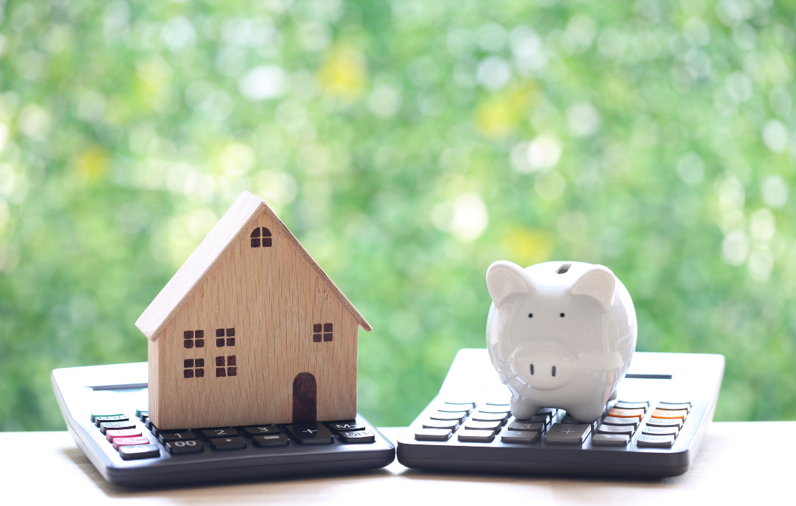 House model and piggy bank on calculators with blurred green background
