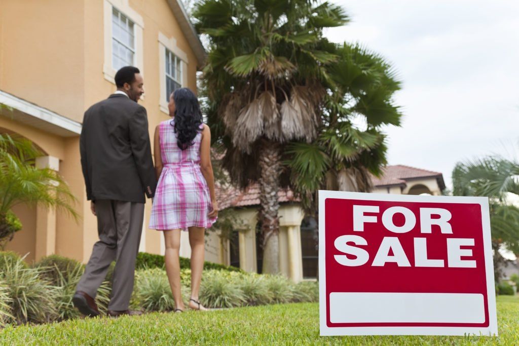 A man and woman standing in front of a for sale sign