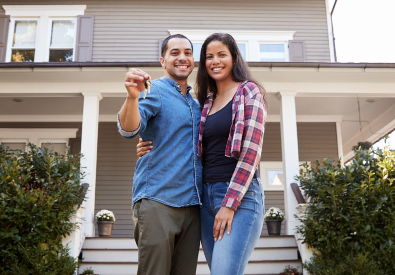 A man and woman are standing in front of a house holding the keys to their new home.