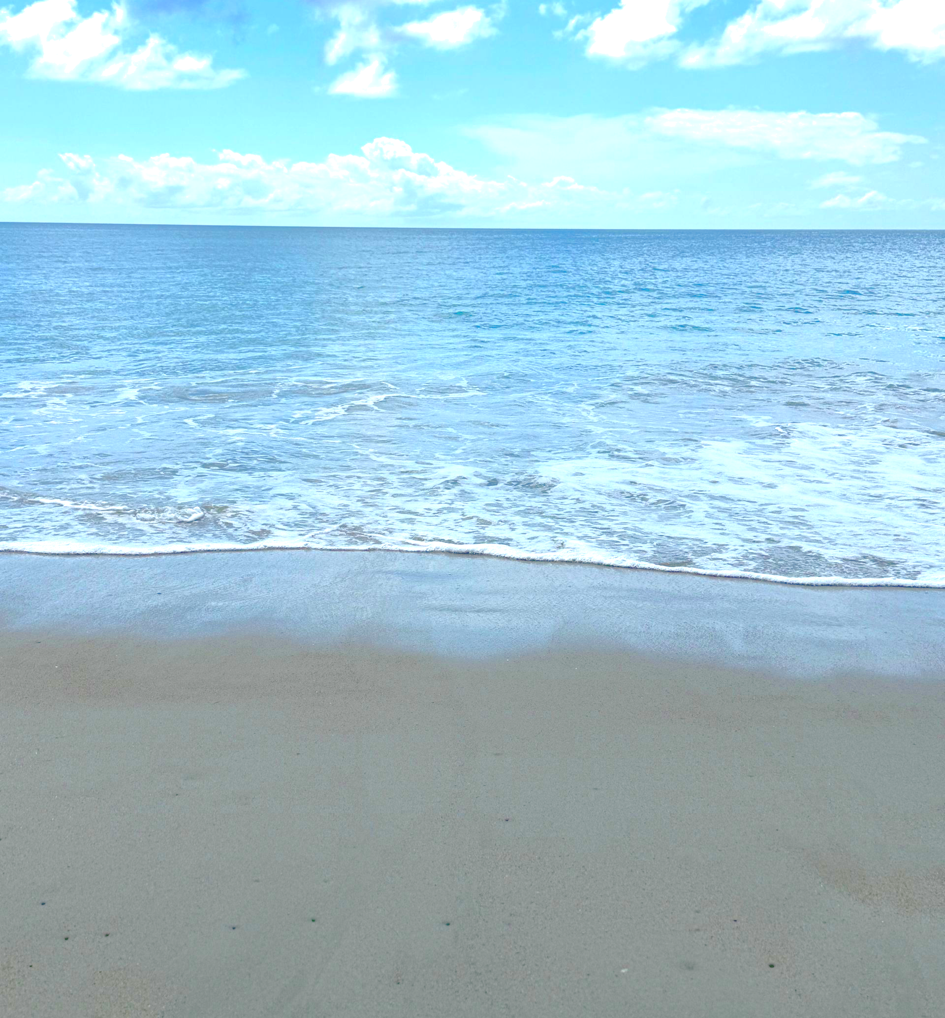 Emerald Isle, NC shoreline with smooth sand, gentle waves, and blue sky.