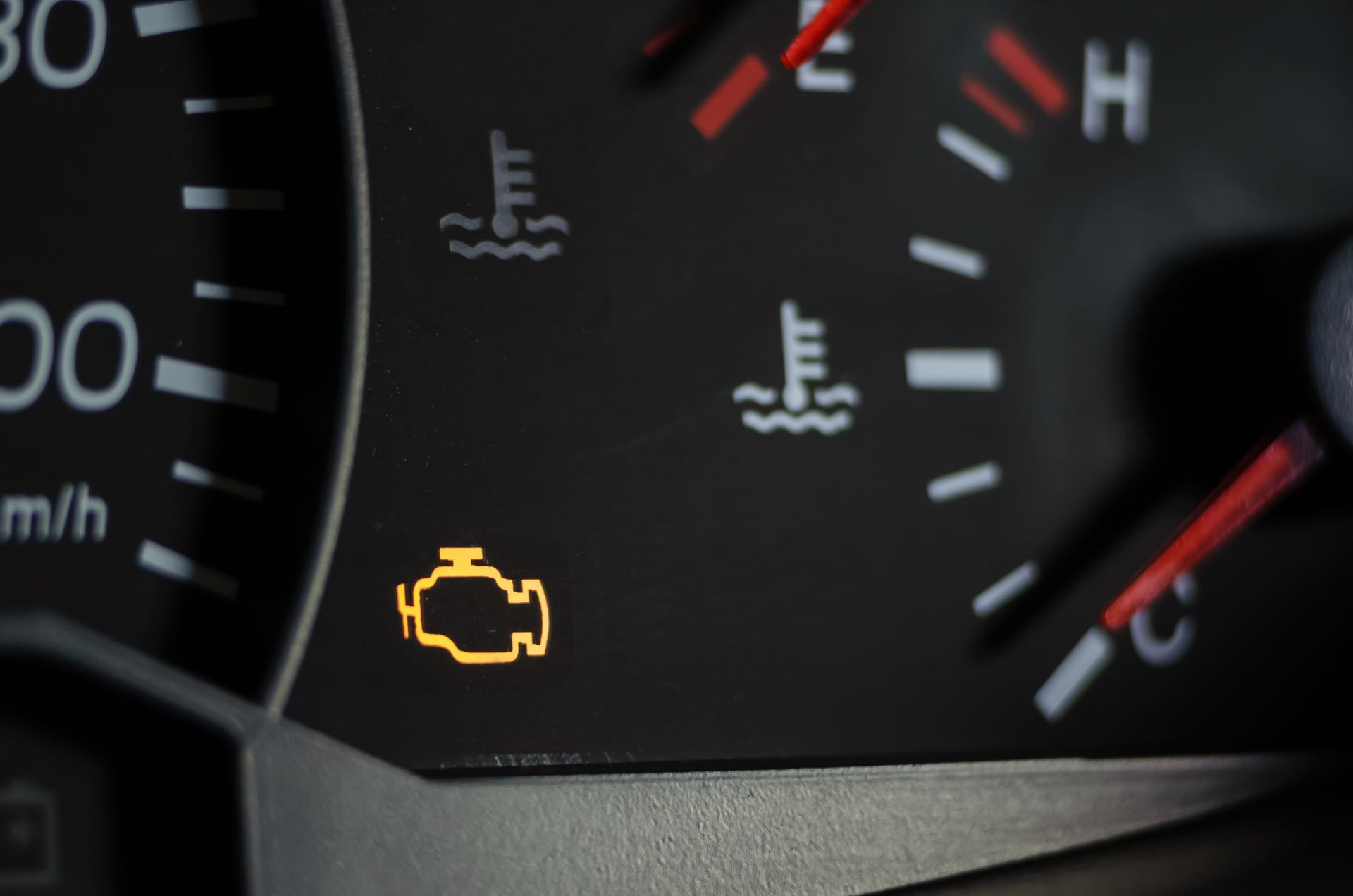 A close up of a car dashboard with a yellow engine light