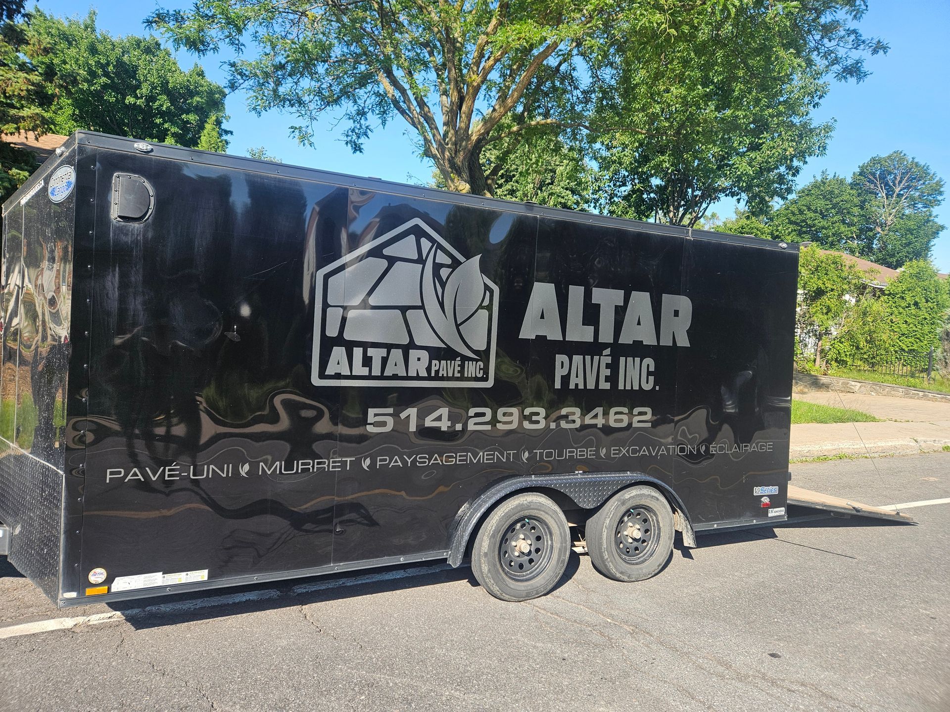Une remorque noire pour le pavage de l'autel est garée sur le bord de la route.