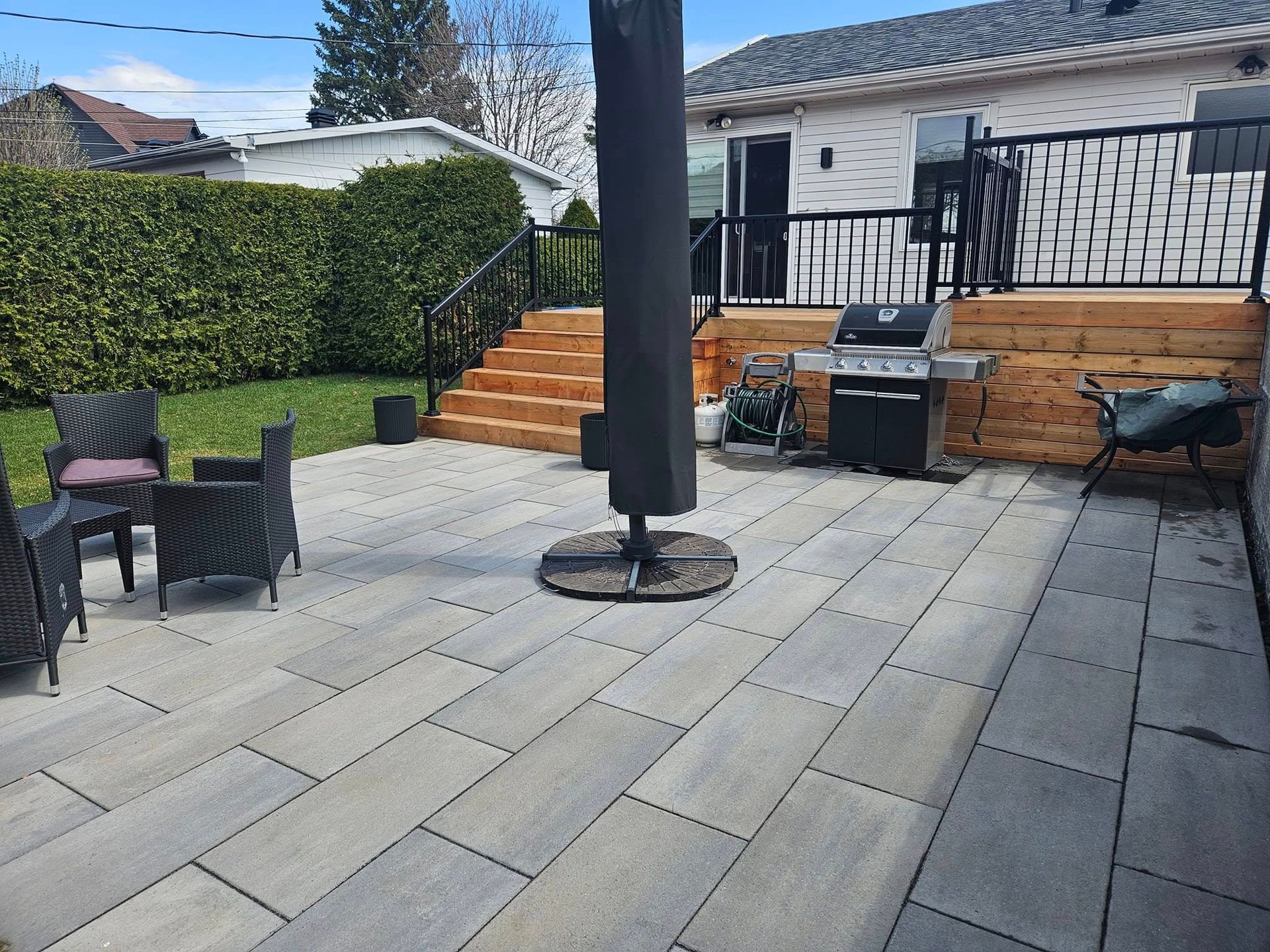 Un patio avec un barbecue et un parasol devant une maison.